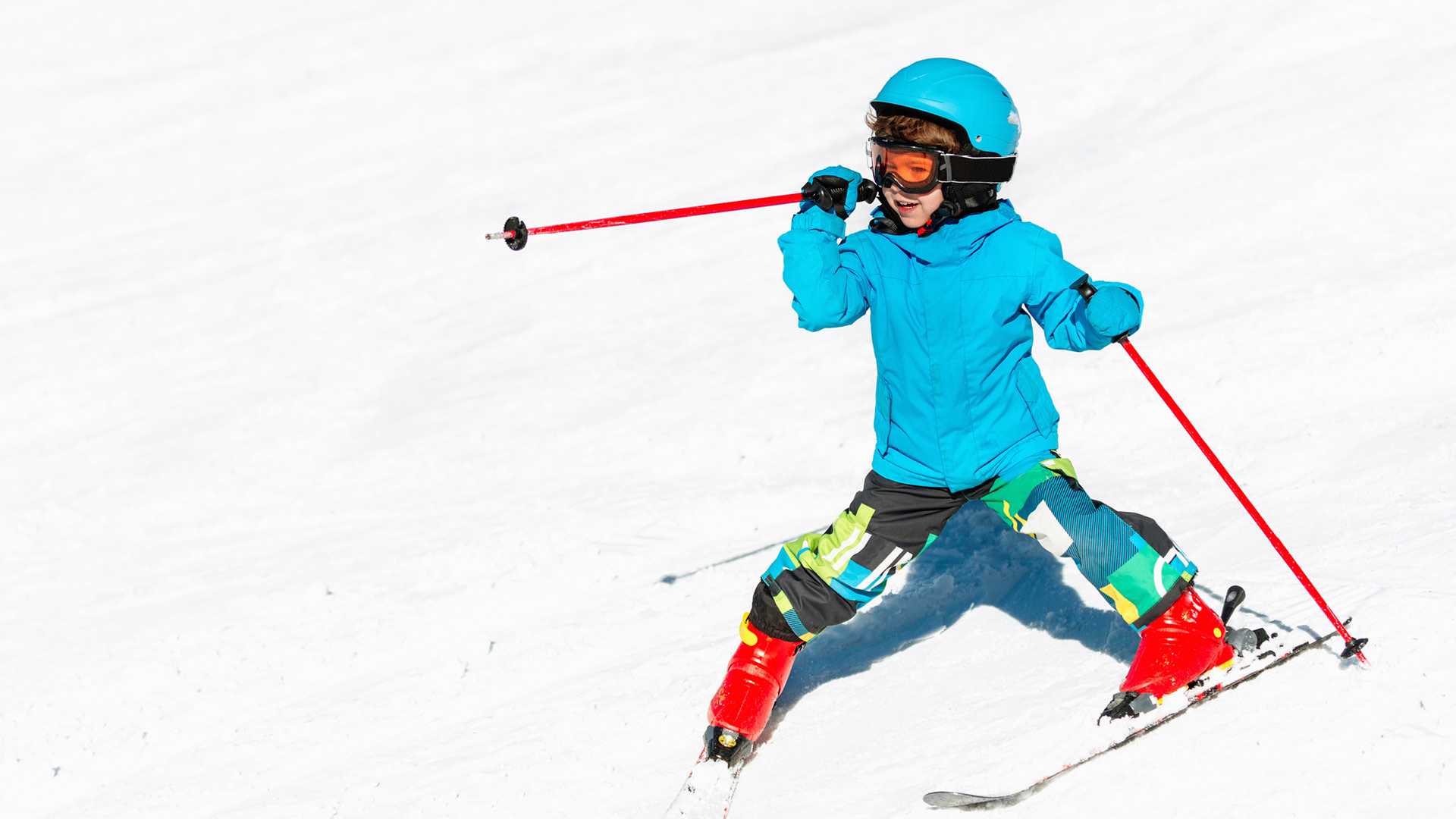 Un petit enfant avec une tenue de ski d’un bleu voyant fait du ski. 
