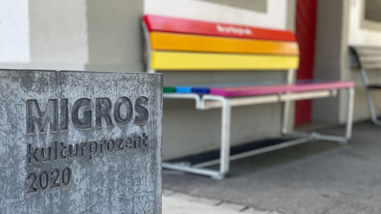 The culture percentage logo depicted on a stone fountain and the rainbow colored bench