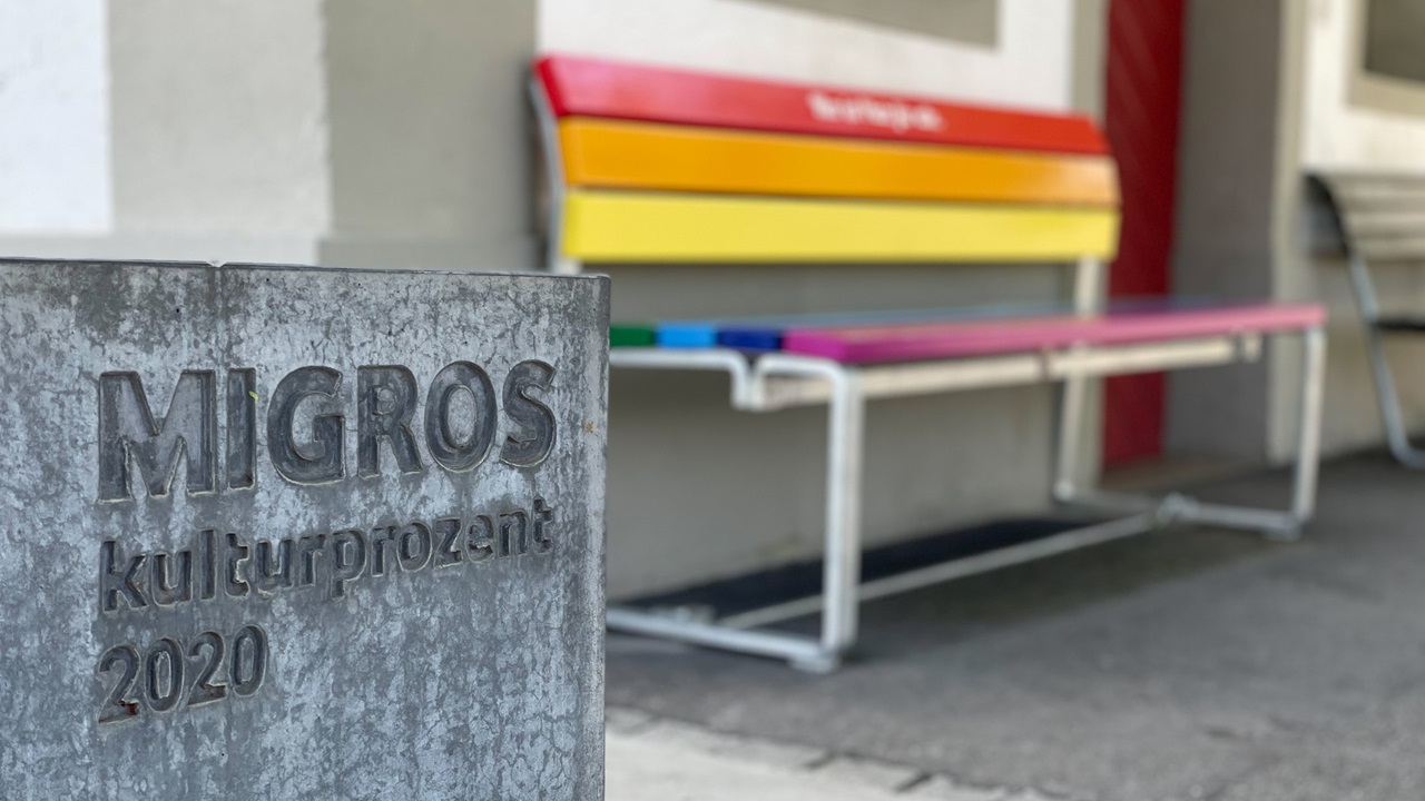 A rainbow colored bench with the inscription 