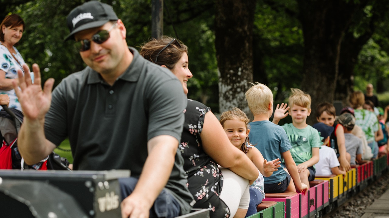 Le petit train fait le tour du parc avec de nombreux visiteurs à son bord. Les enfants agitent la main.
