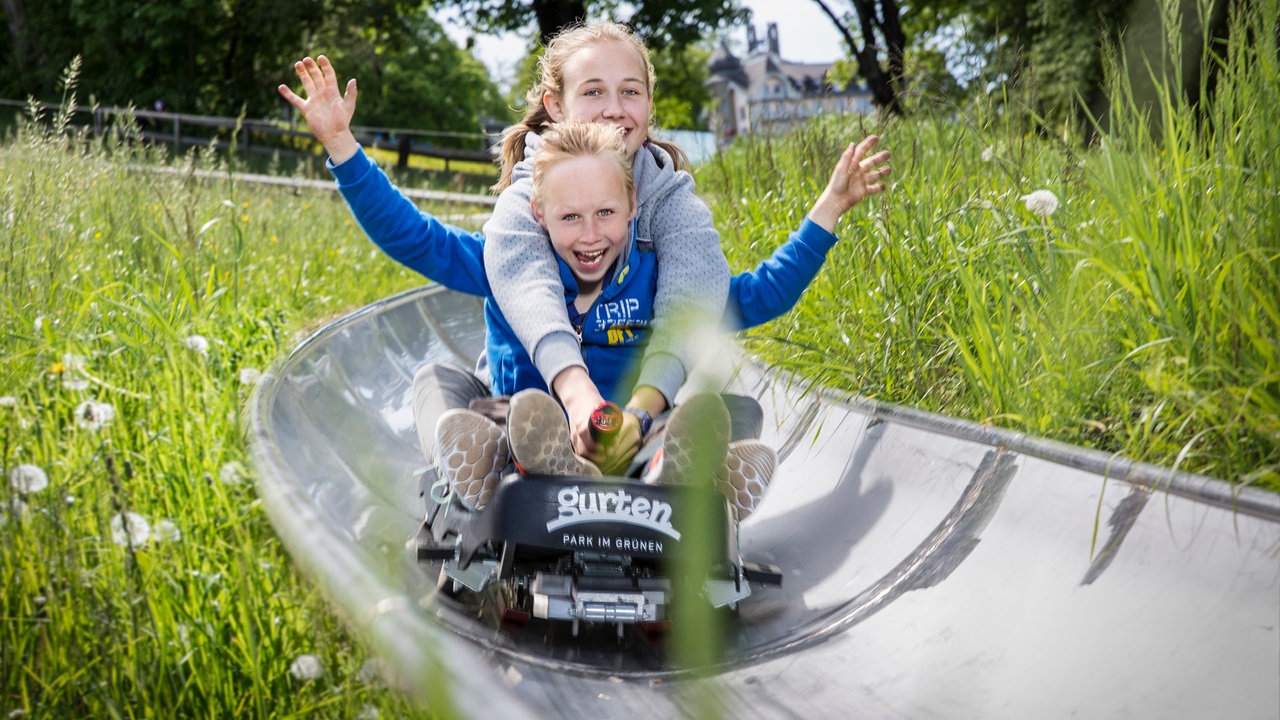 Zwei Kinder fahren lachend die Sommerrodelbahn hinunter.