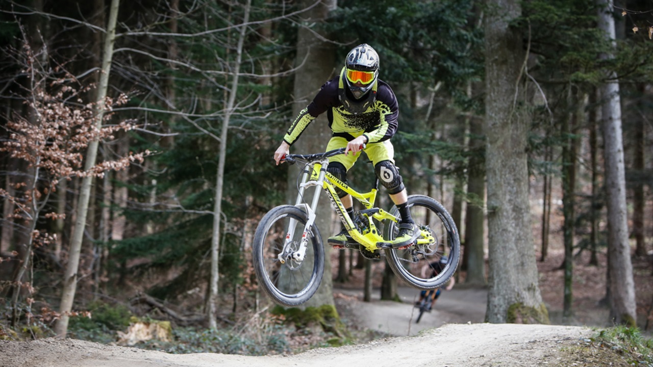 A downhill cyclist jumping a meter into the air over a dirt jump. 