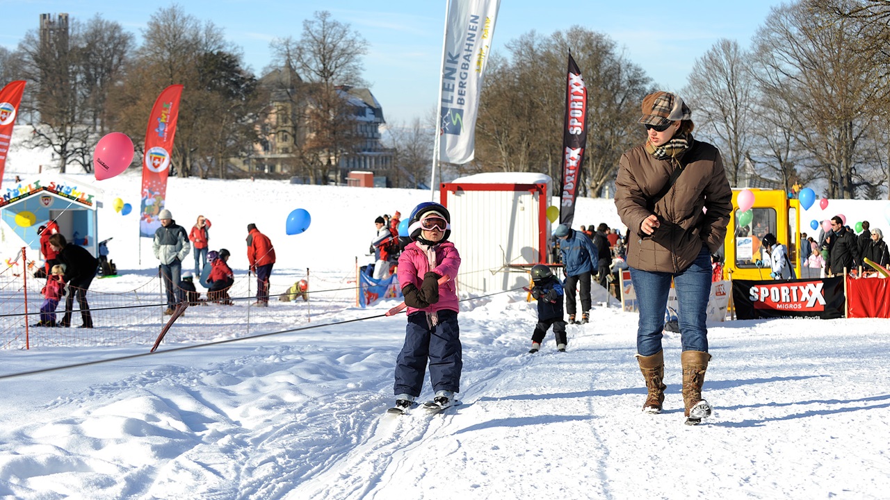 Der Kinderskilift zieht ein Kind mit Skis die Piste hinauf. 