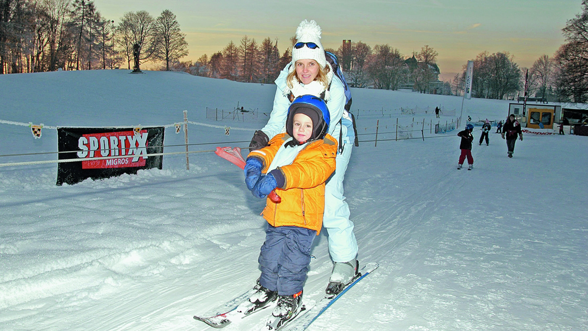 Ein Kind und eine Frau werden mit dem Skilift die Piste hinaufgezogen. 