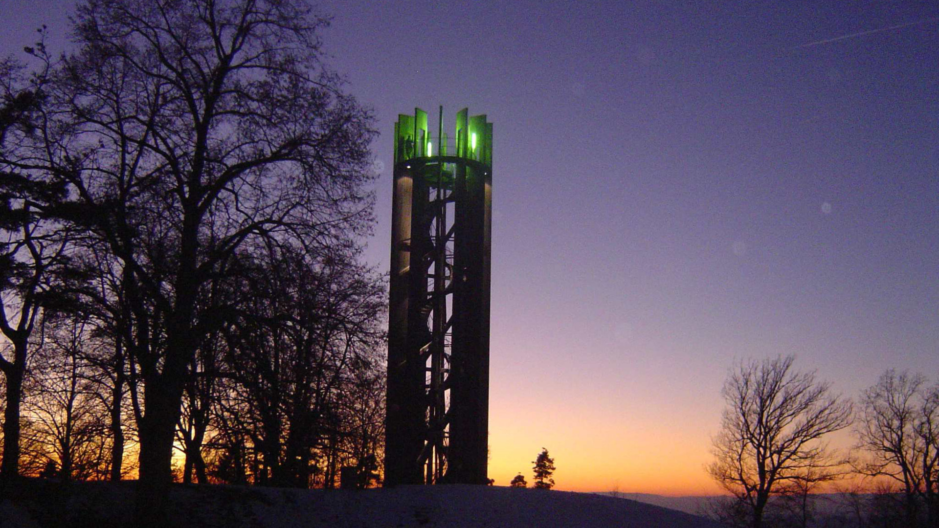 Der 22 Meter hohe Aussichtsturm auf dem Gurten leuchtet mit grünem Licht während des Sonnenuntergangs.
