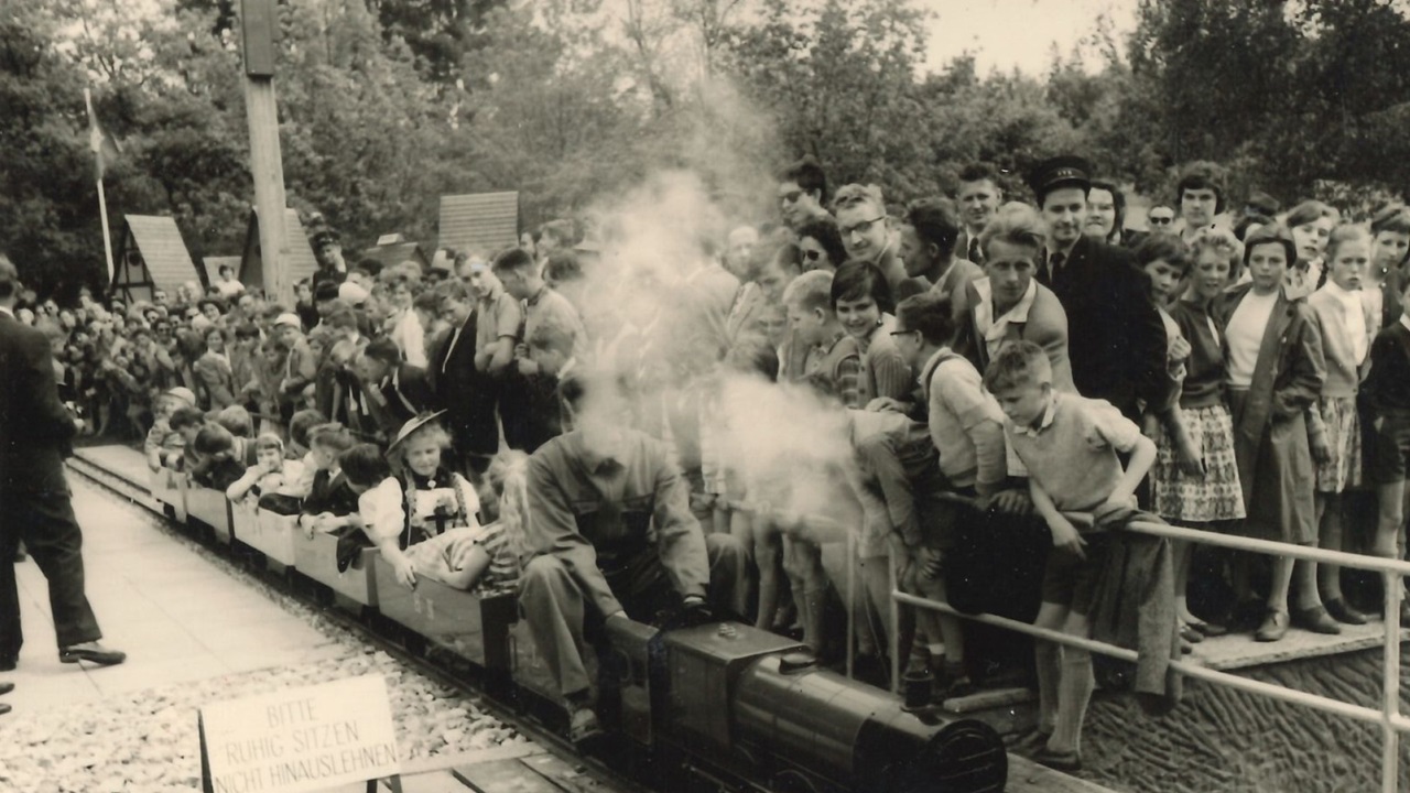 A nostalgic picture of the miniature railway. A hoard of kids standing around the miniature railway.