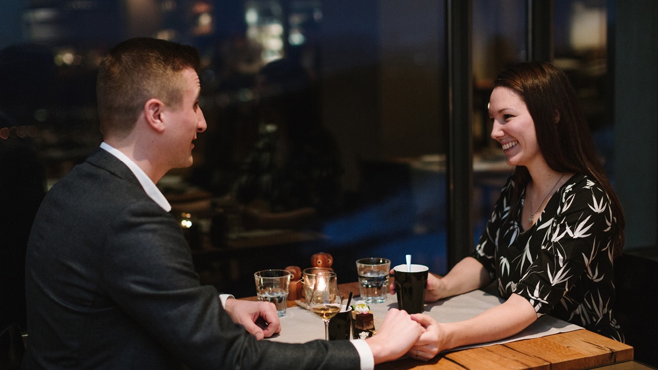 Un couple d’amoureux se tient par la main à une table avec vue