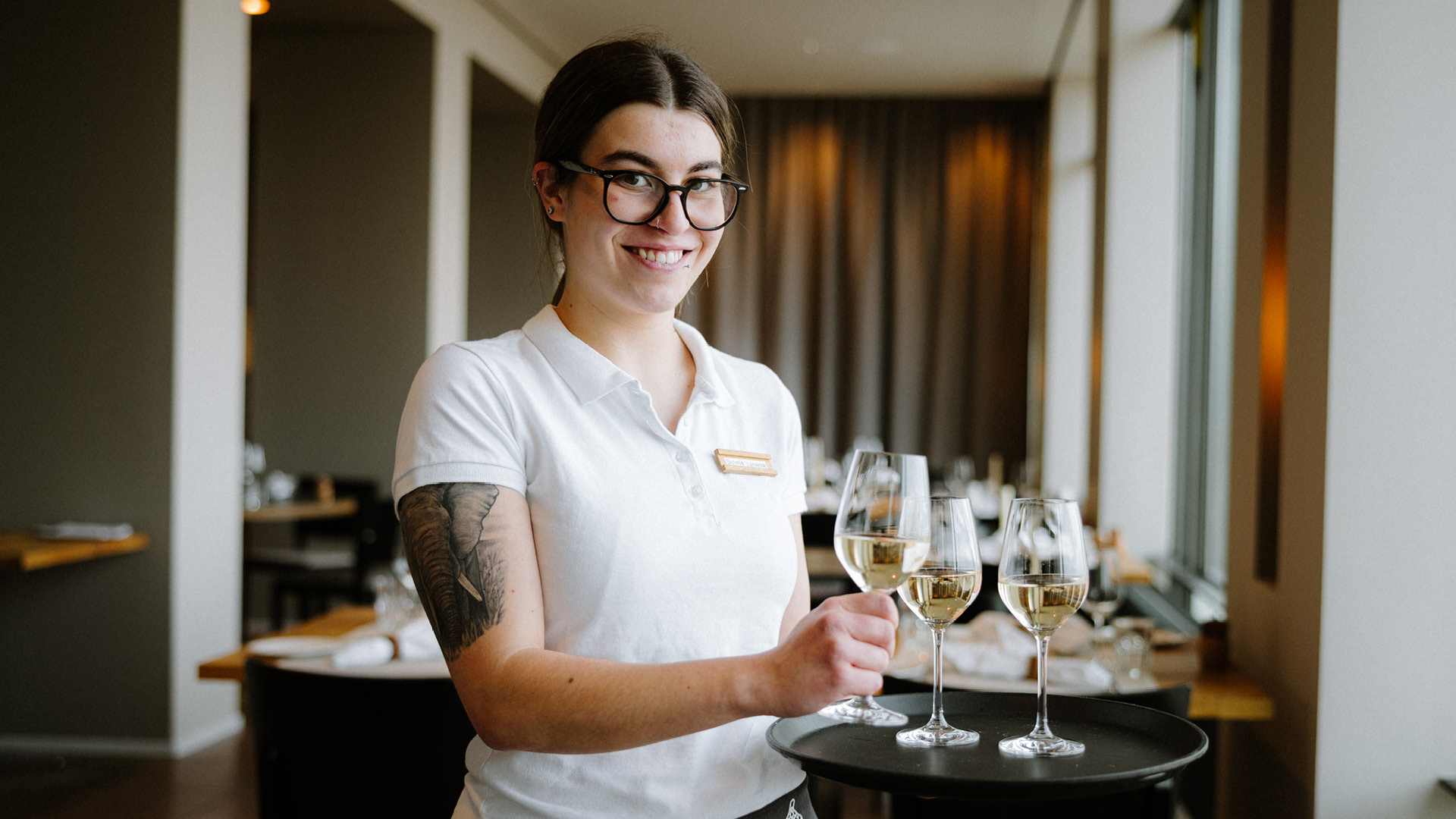 Une serveuse porte un plateau avec des verres à vin blanc au restaurant Gurtners