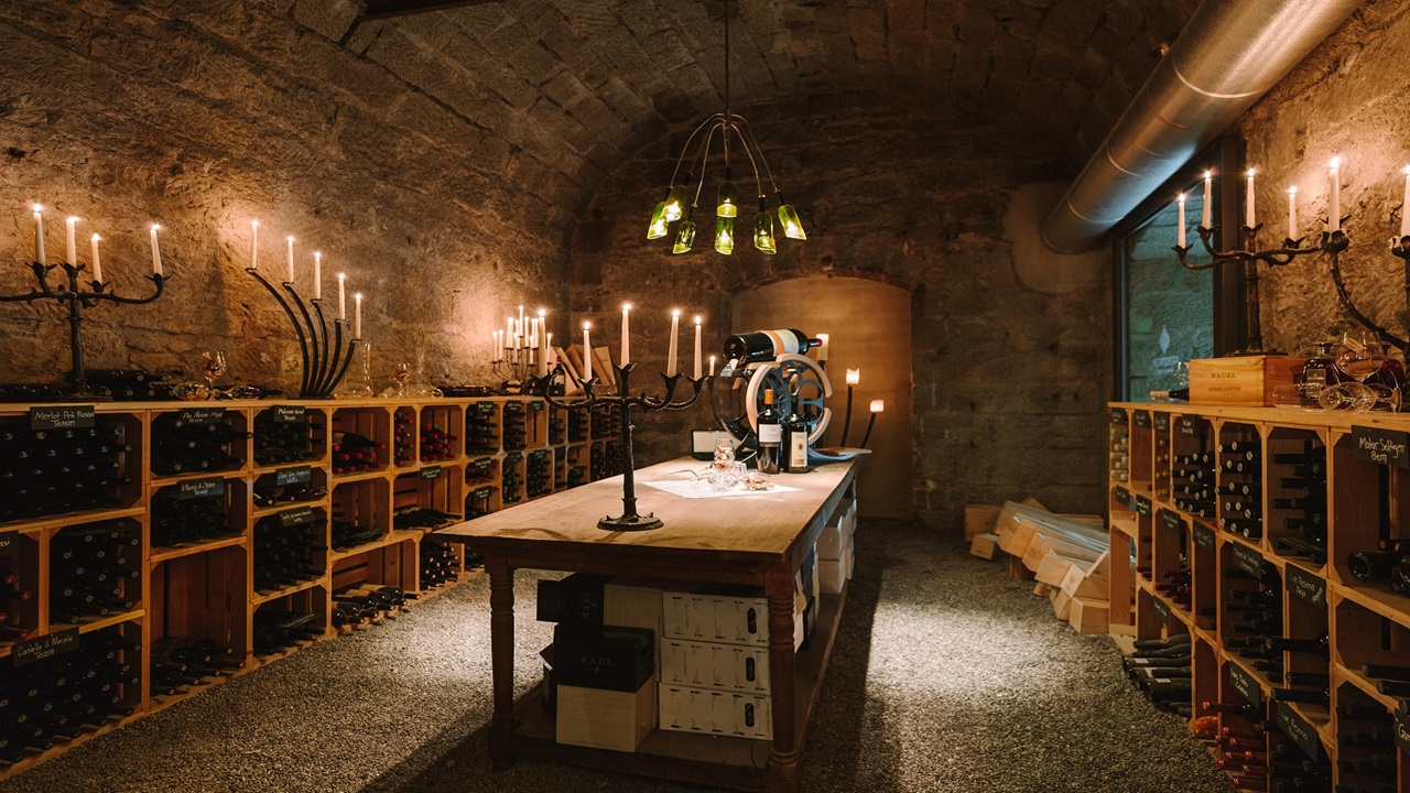 Rustic wine cellar with a large wooden table. The cellar is lit by candles.