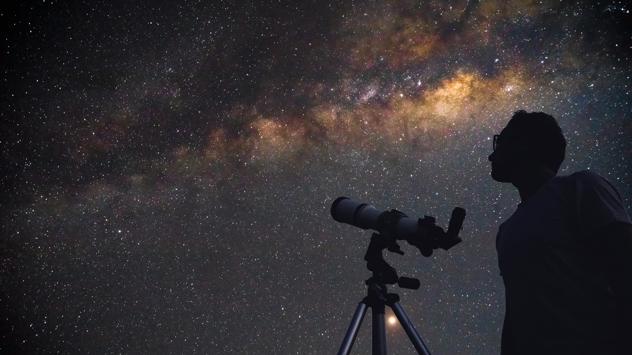 Ein Mann schaut durch ein Teleskop die Sternschnuppennacht an.