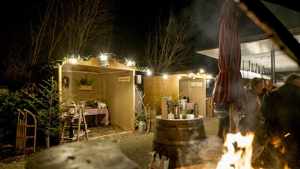 Village d’hiver sur le Gurten avec des chalets illuminés, un feu et des visiteurs de nuit.