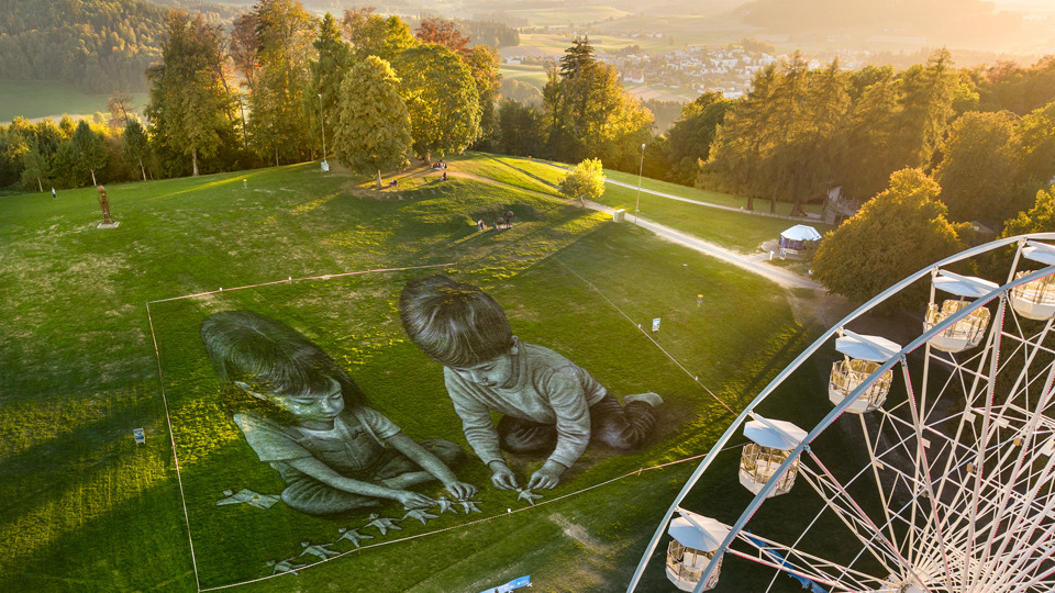 Two children laying out origami figures in Saype's monumental fresco.