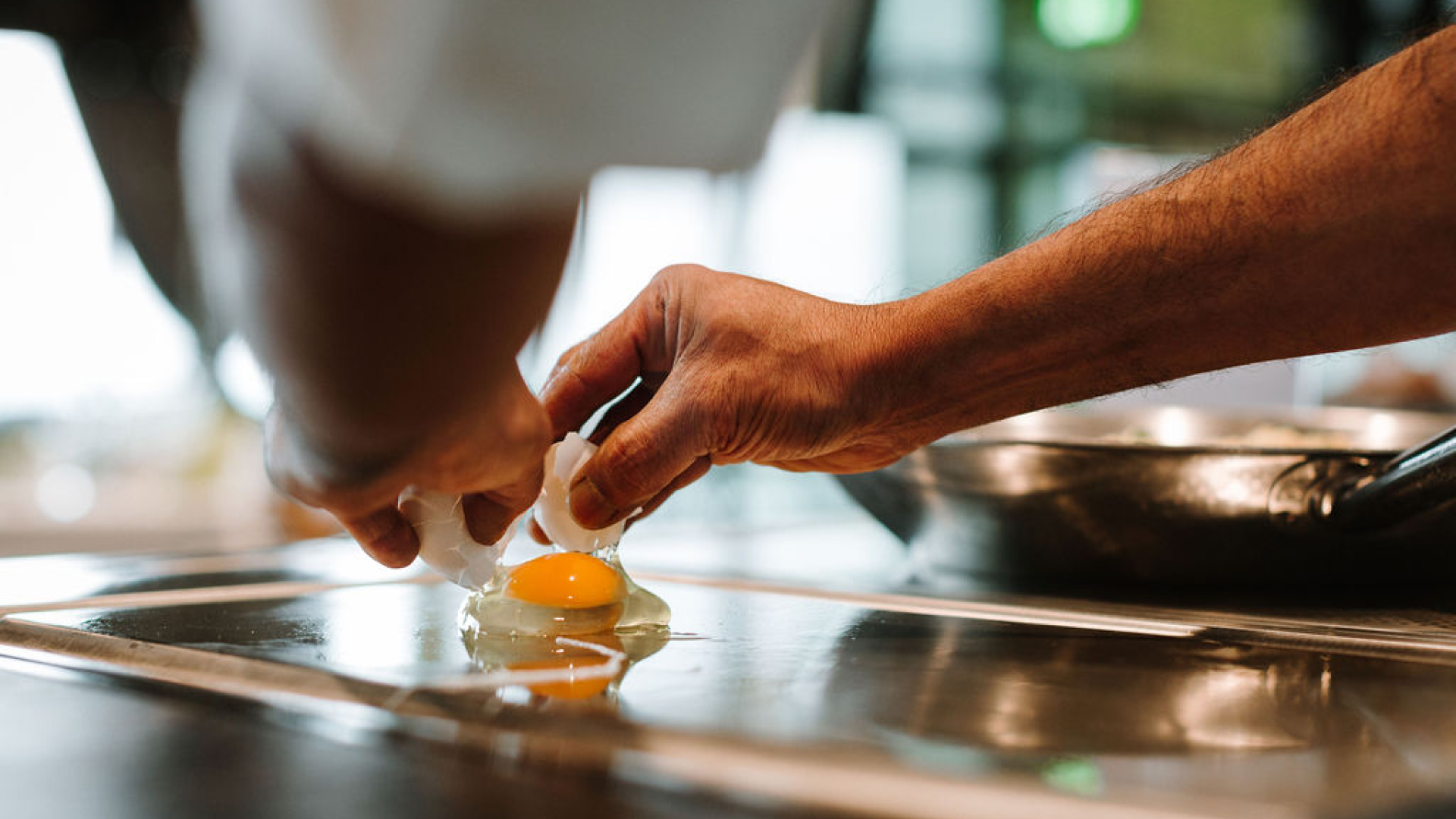 Une personne qui casse un œuf cru dans une poêle pour le faire cuire.