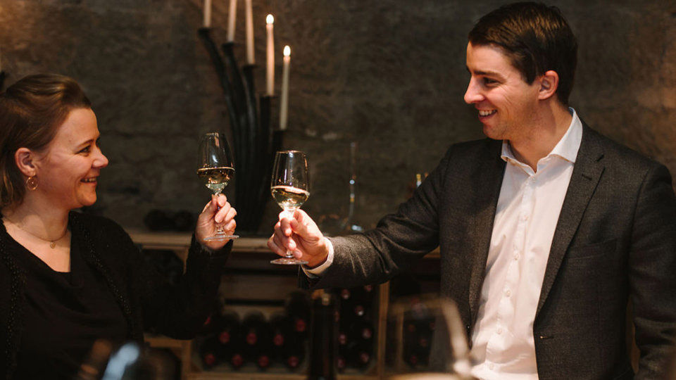 Deux personnes trinquent avec un verre de vin blanc dans la cave à vin.