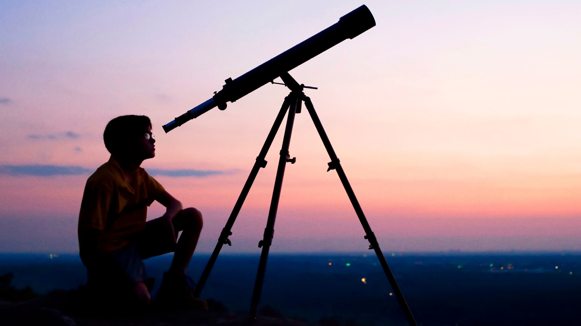 Un enfant assis devant un ciel rouge observe le ciel à travers un long télescope.