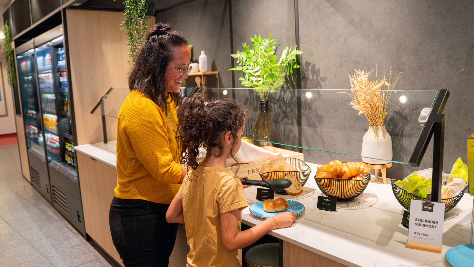Two people at brunch in Huusbüffe putting bread on their plates. They are both wearing yellow tops.