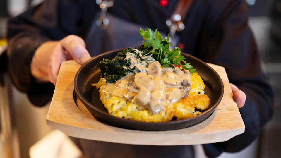 The chef at the self-service restaurant Huusbüffe is holding a rösti with mushrooms and spinach in his hands.