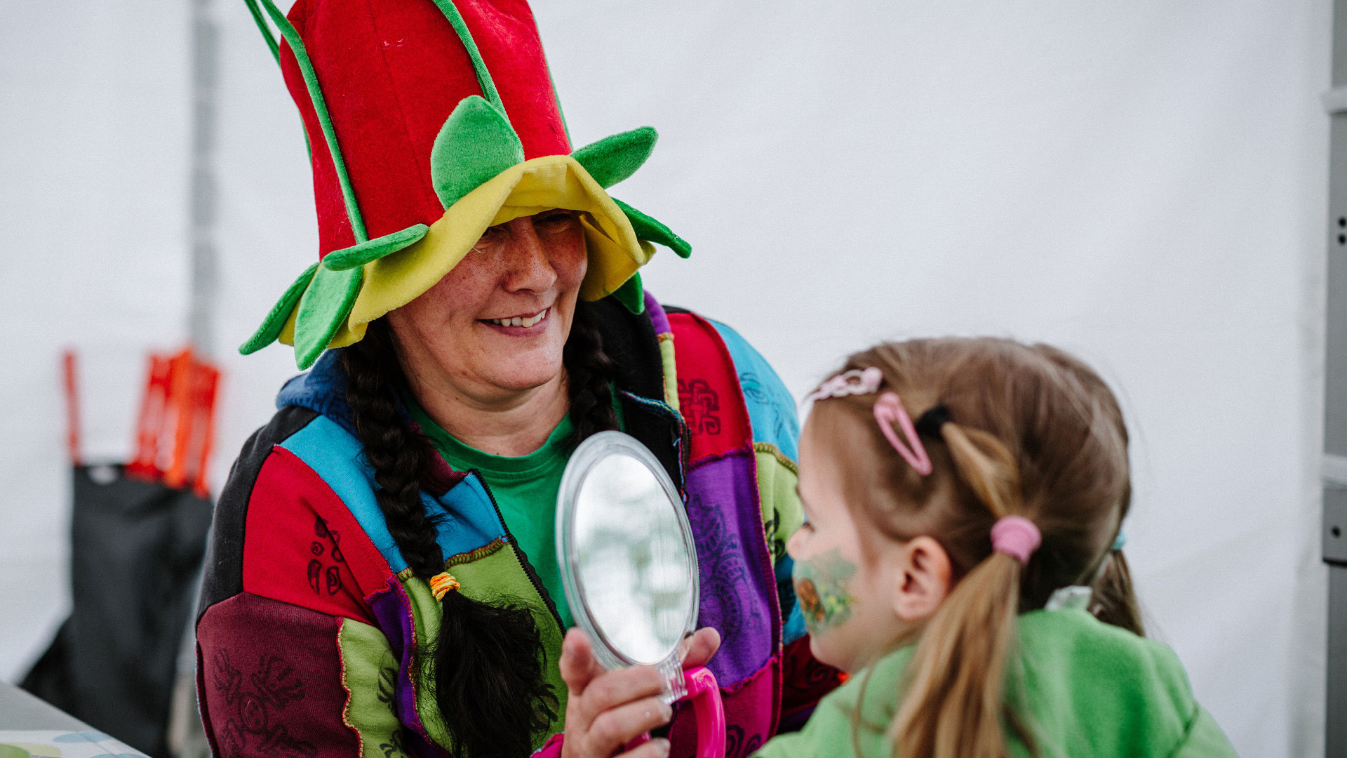 Serafina Eulenstein zeigt einem Kind sein geschminktes Gesicht mit einem Spiegel.
