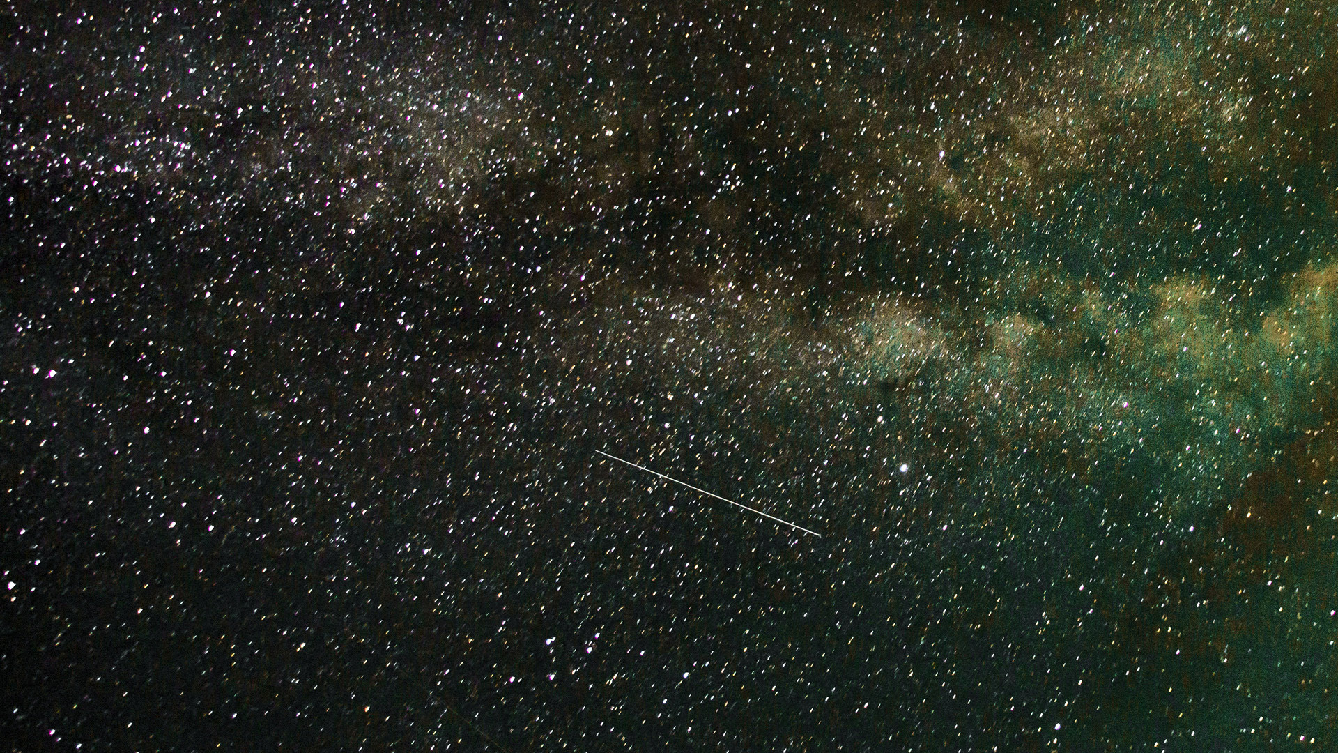 Starry sky with a greenish tint. A shooting star can be seen.