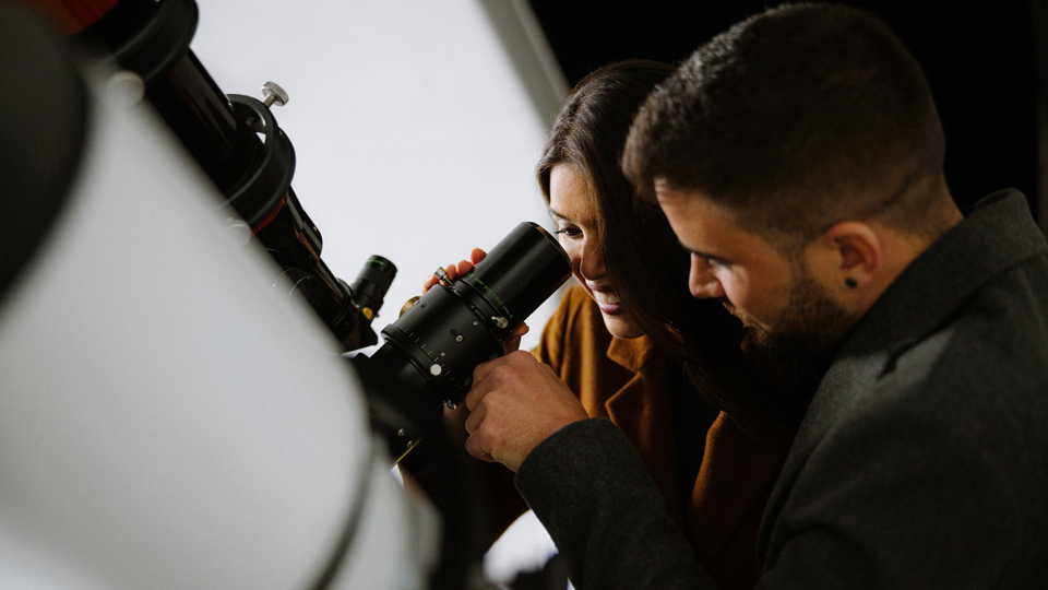 Une femme regarde à travers le grand télescope de l'observatoire du Gurten et un homme se tient à côté d'elle.