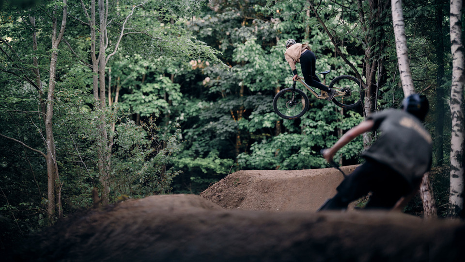Zwei Mountainbiker fahren Gurtentrail, einer macht Sprung über Schanze