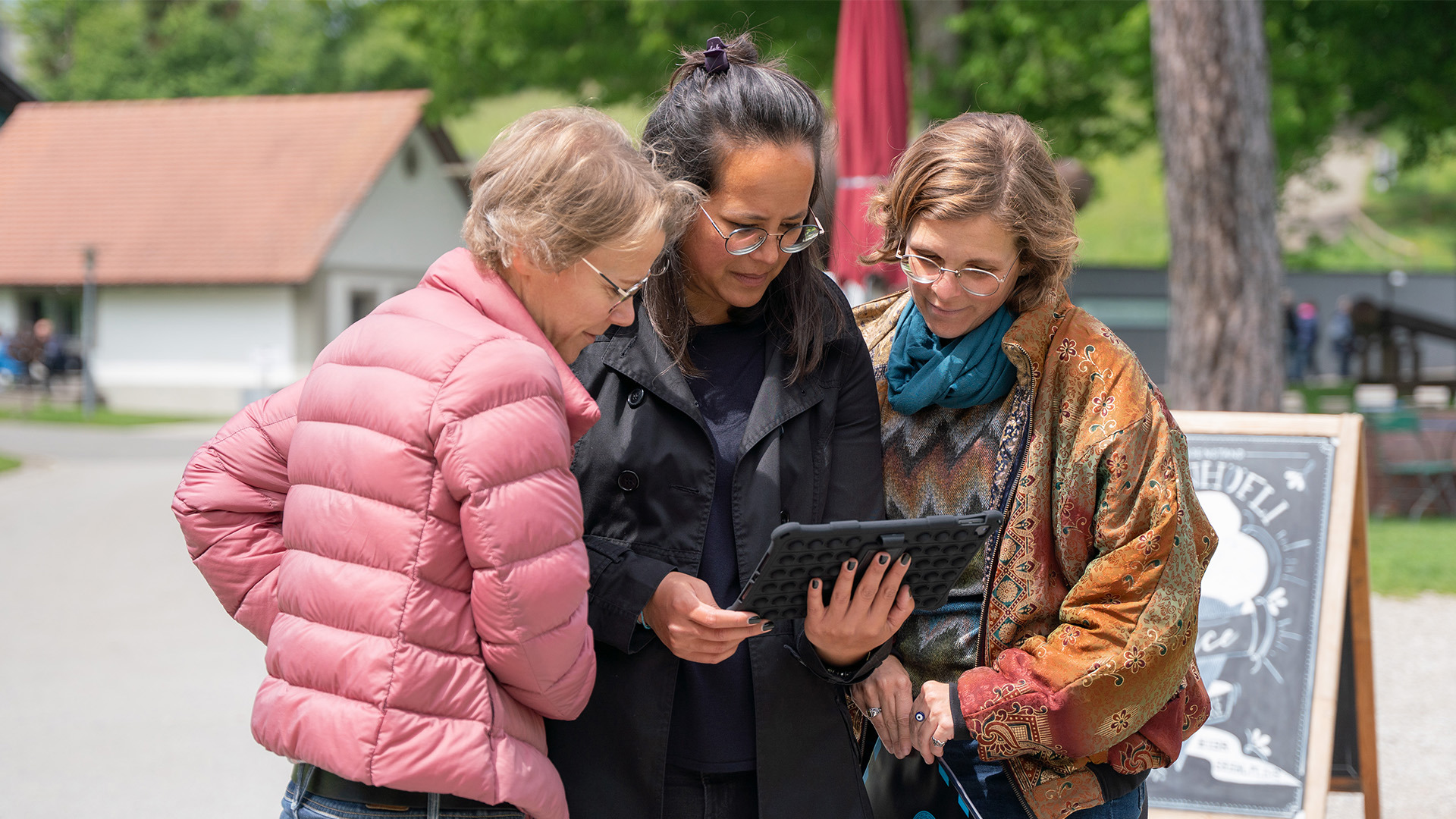Drei Frauen spielen mit einem Tablet in der Hand das Outdoor Escape Game