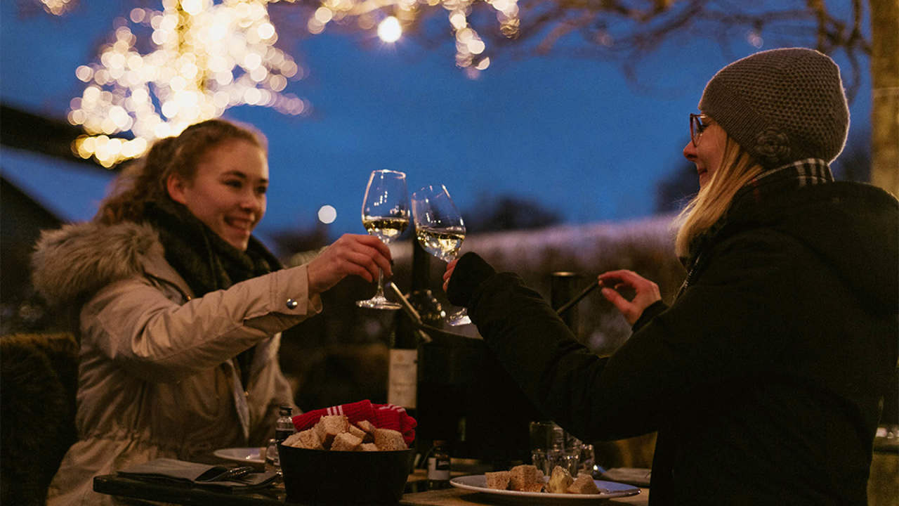 Deux personnes trinquent avec un verre de vin blanc autour d'une fondue à la pleine lune.