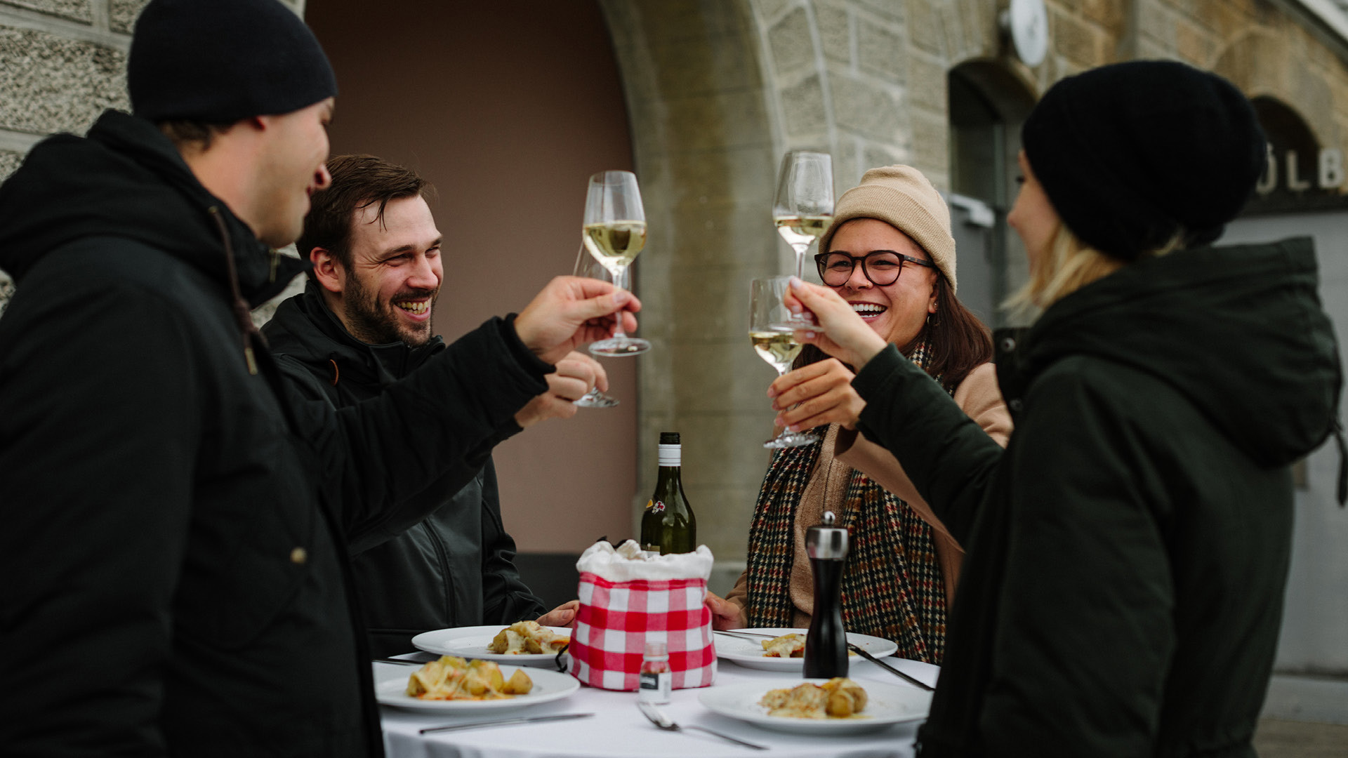 Vier Personen beim Outdoorfondue stossen mit Weisswein an.