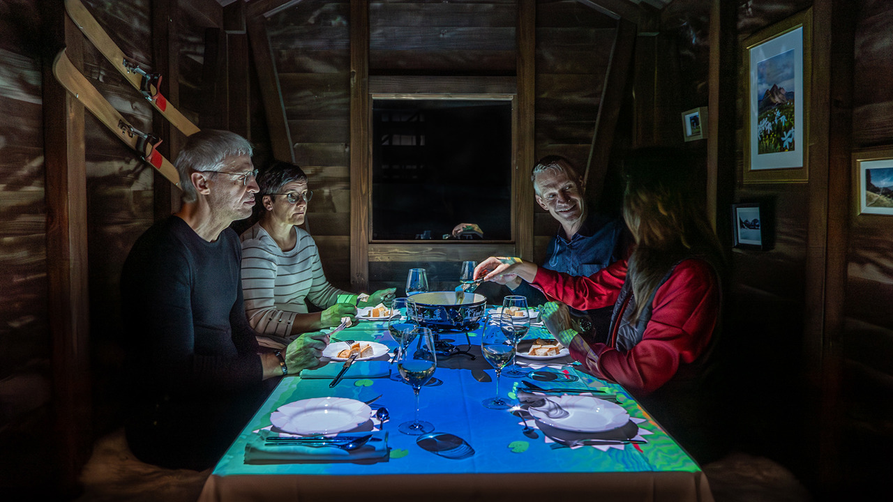 Four people are eating fondue in a wooden chalet.