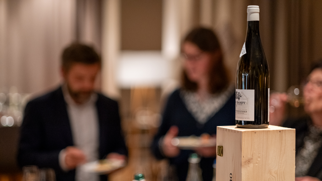 A bottle of red wine is sitting on Gurtner's kitchen table; behind it, the two winemakers are talking
