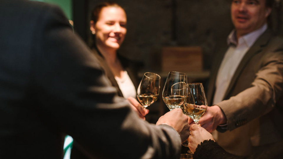 Quatre personnes trinquent avec un verre de vin blanc dans la cave à vin.