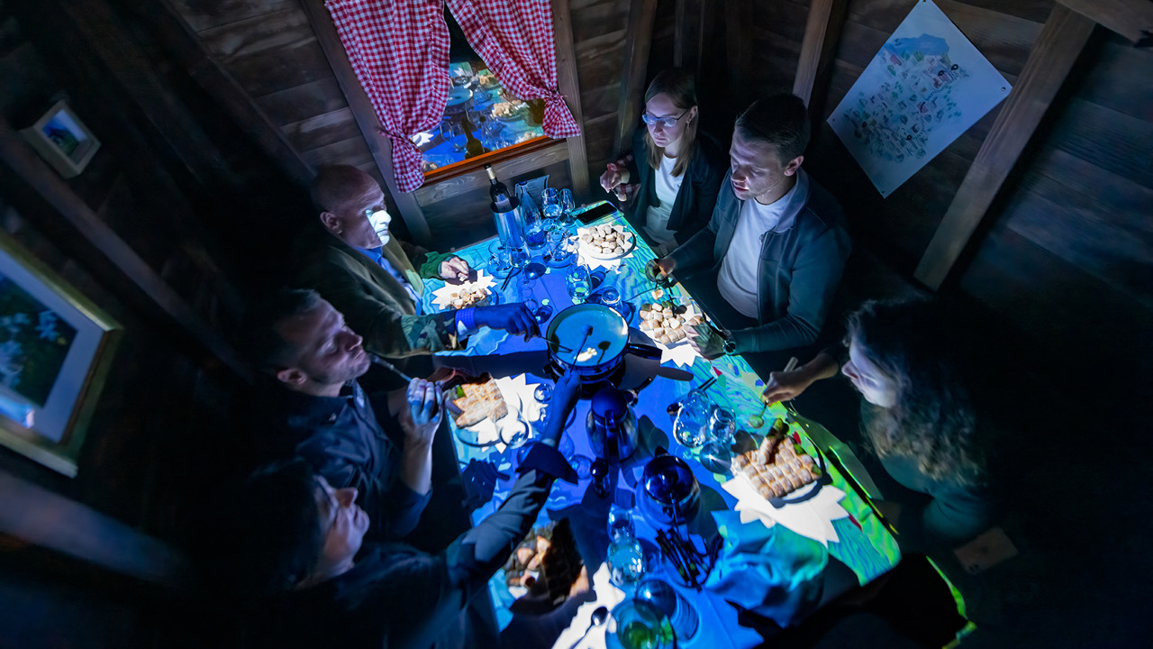 Six people are eating fondue in a small wooden chalet.