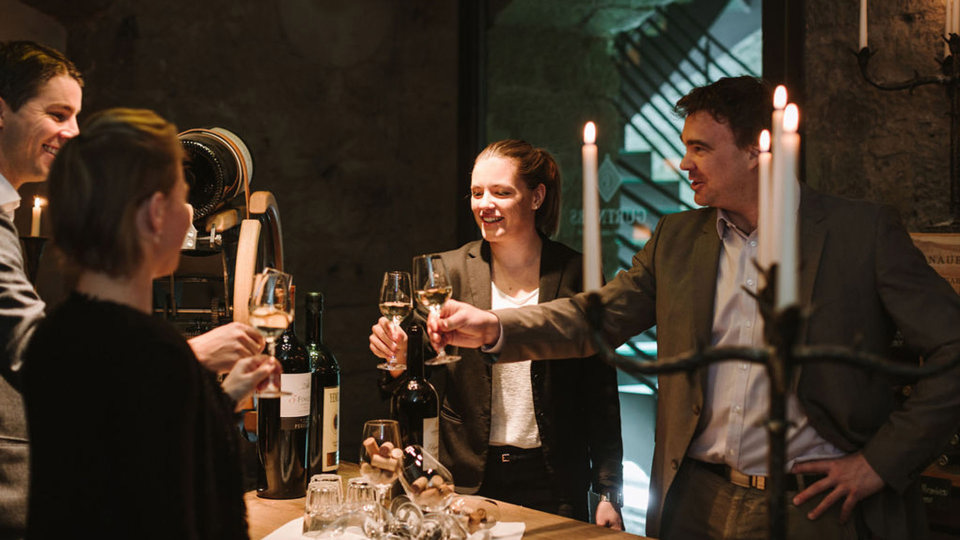 Quatre personnes trinquent avec un verre de vin dans la cave à vin voûtée.