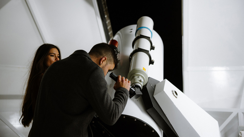 Un homme regarde à travers le télescope de l'observatoire du Gurten et une femme l'observe.