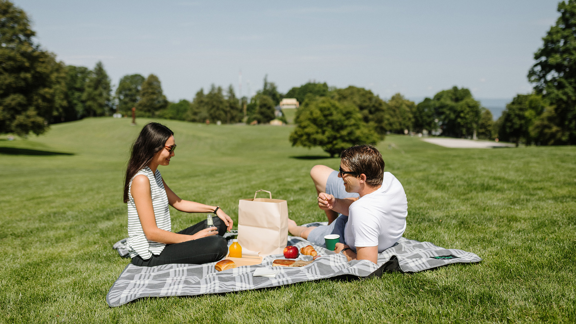 Deux personnes dégustant le brunch to go sur une couverture de pique-nique dans une verte prairie.