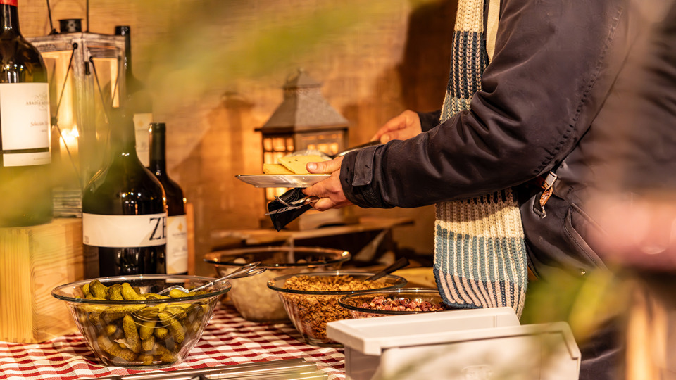 Une personne compose une assiette de raclette et d’accompagnements à un buffet dans le village d’hiver sur le Gurten.