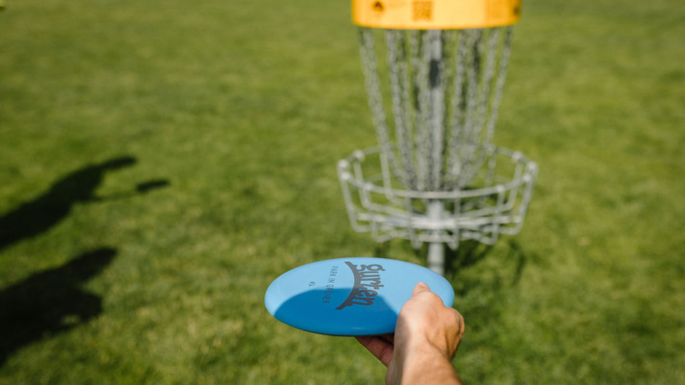 Une personne tient un frisbee dans la main, avec un panier de disc golf en arrière-plan.