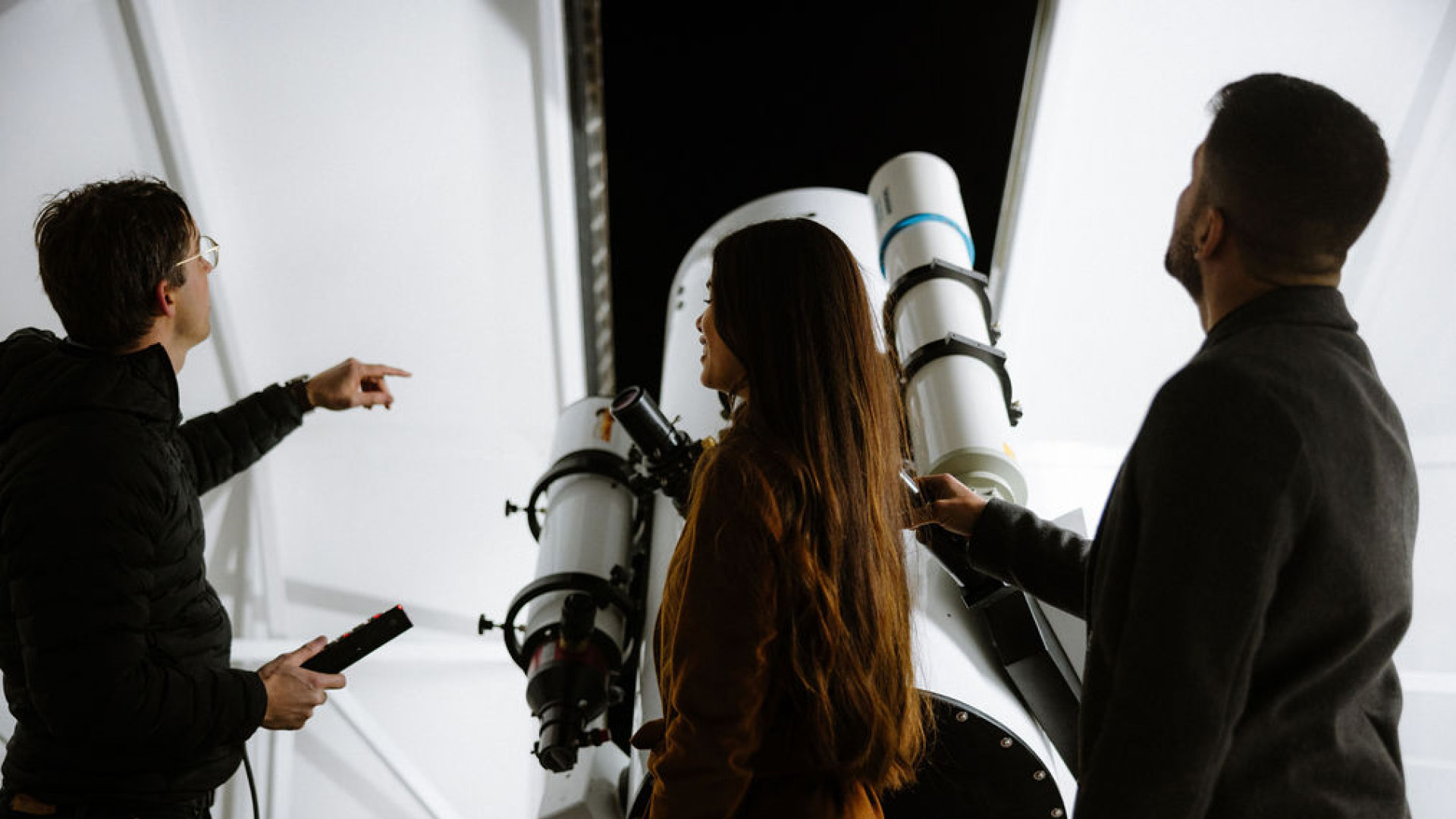Three people are standing in the observatory and an expert is explaining the sky to them.