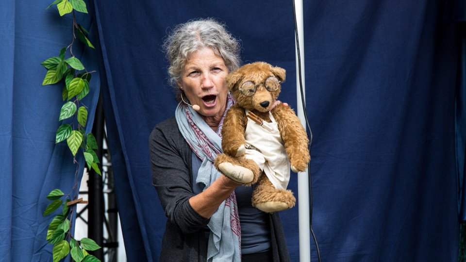 A woman playing with a teddy bear wearing glasses.