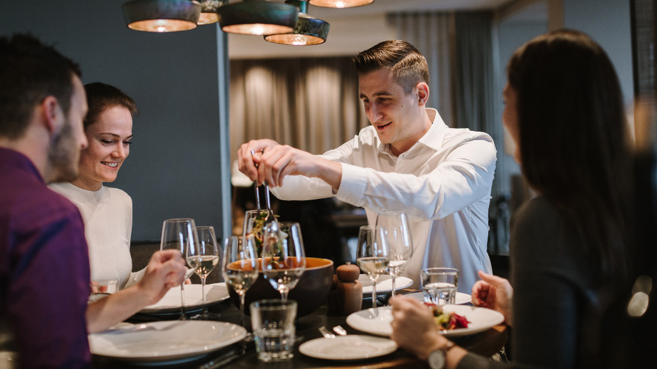 Four people sitting at a table, serving themselves salad from a salad bowl. They are sitting in the Stübli at Restaurant Gurtners on the Geniessermontag.