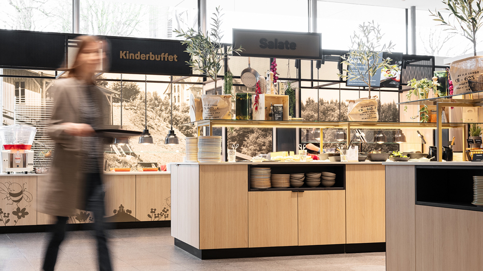 A woman walks through the Huusbüffe self-service restaurant carrying a serving tray.