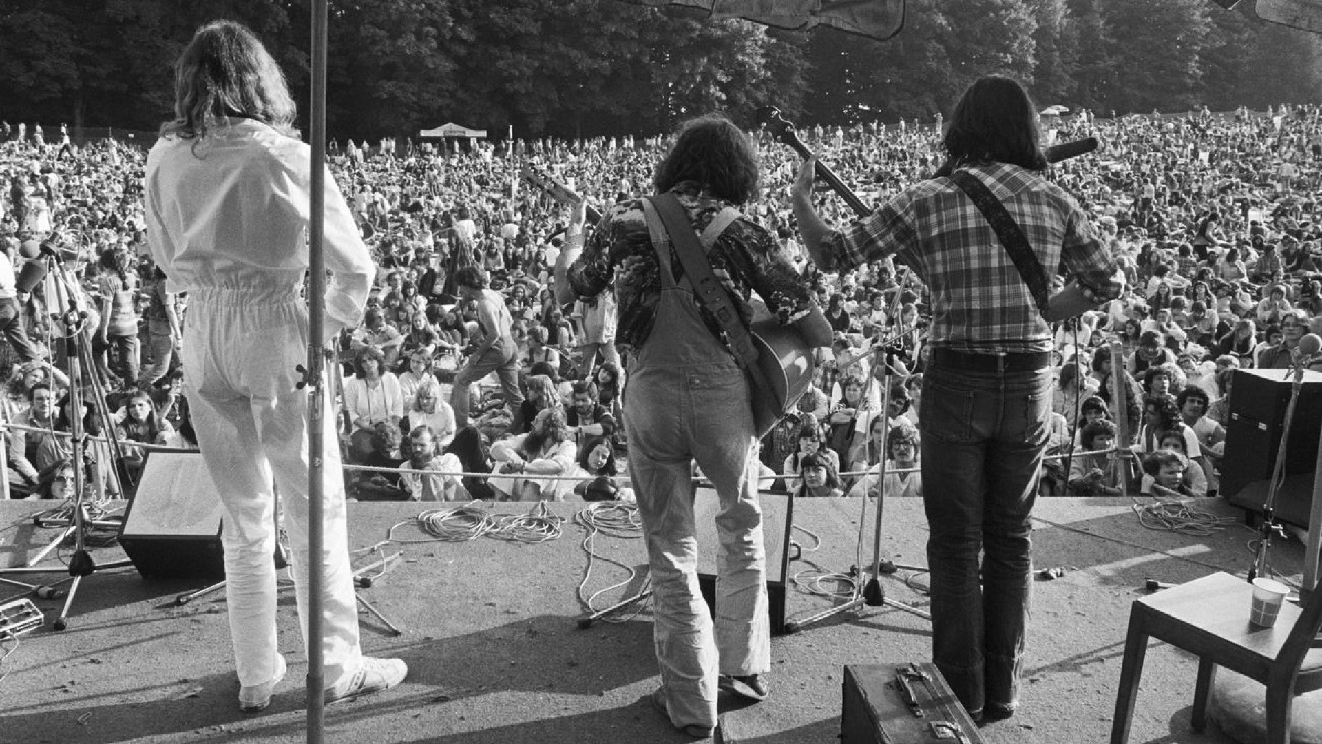 Drei Musiker auf der Bühne vom ersten Gurtenfestival 1977 mit Publikum im Hintergrund.