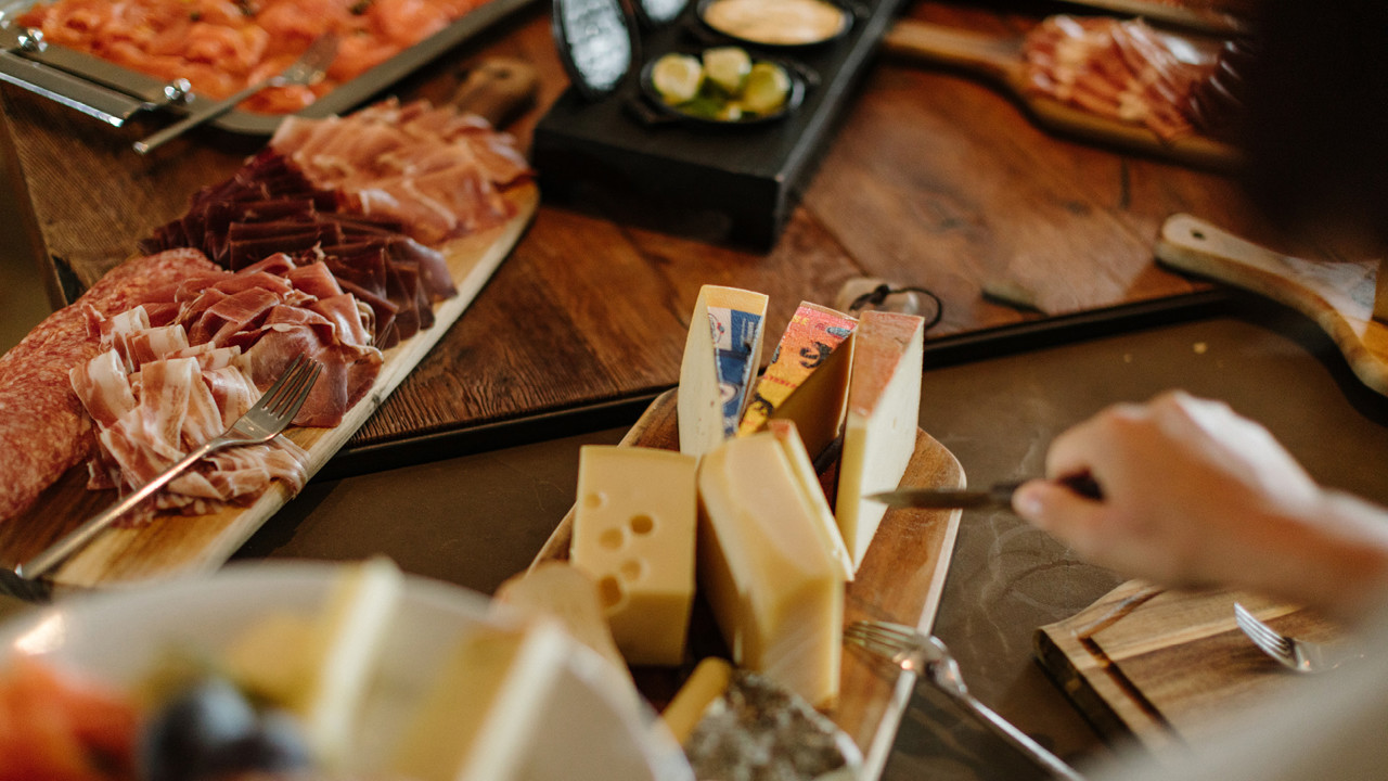 A person cutting cheese from a wooden board with a knife.
