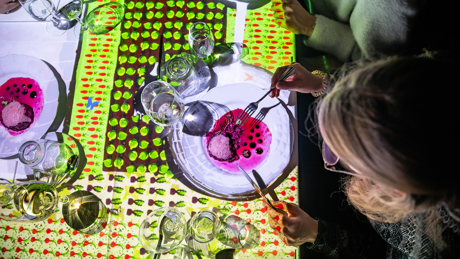 A woman eats soup at a table with immersive lighting.