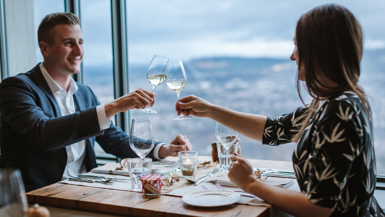 Two people sitting at a table and toasting with a glass of white wine during a candlelight dinner.