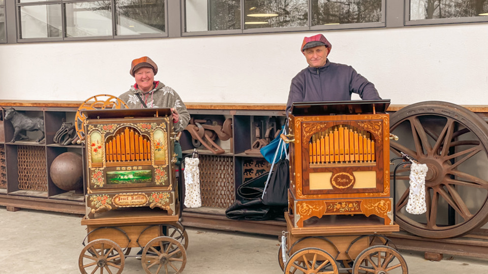 Two people are turning barrel organs.