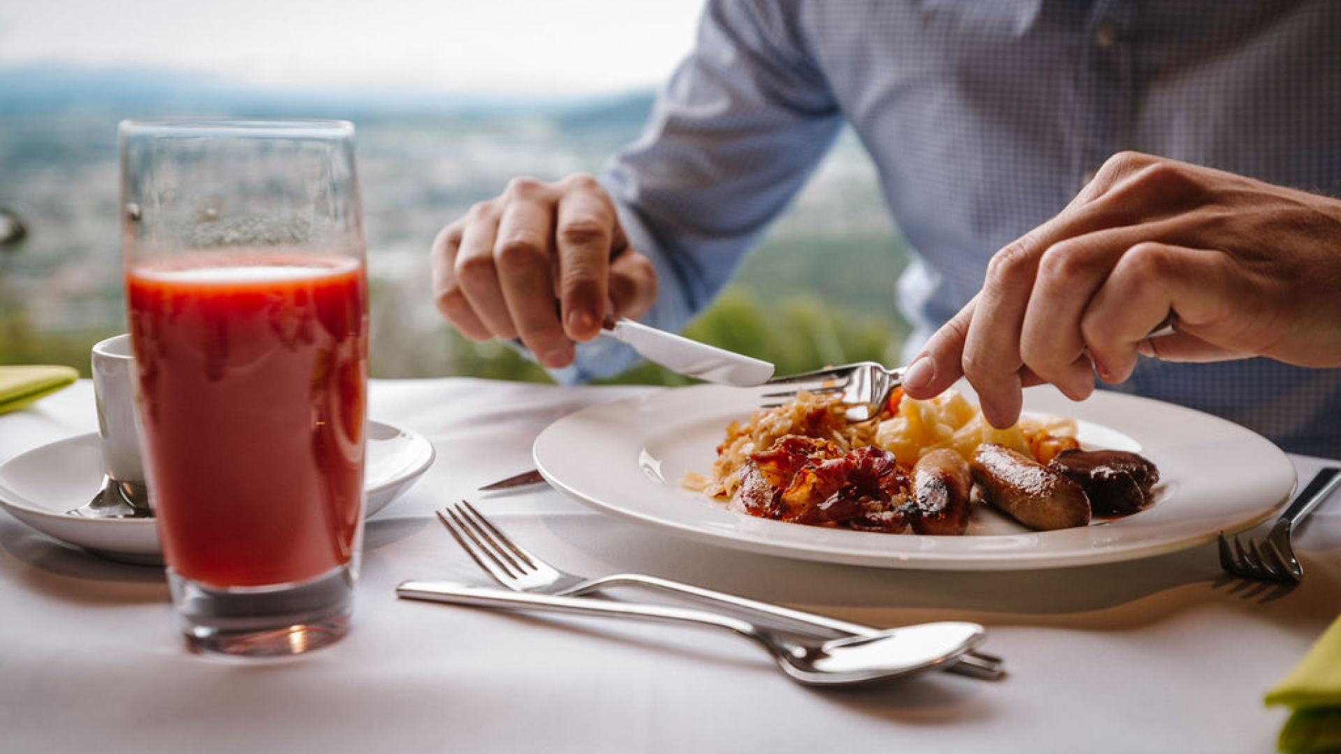 A photo of a person enjoying a plate of treats from the Verwöhnbrunch. The person is wearing a blue button-down shirt, and a glass of blood orange juice is next to the plate.