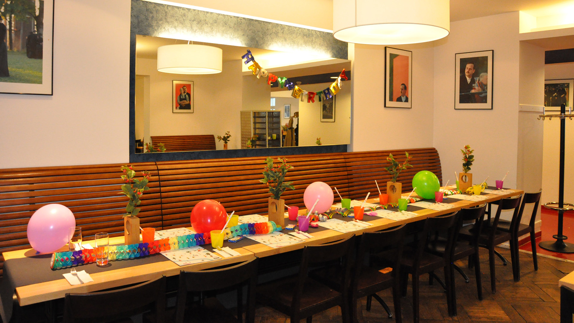 Une table d'anniversaire festivement décorée dans le Huusbüffe avec des ballons, des serpentins, des fleurs et des gobelets colorés.