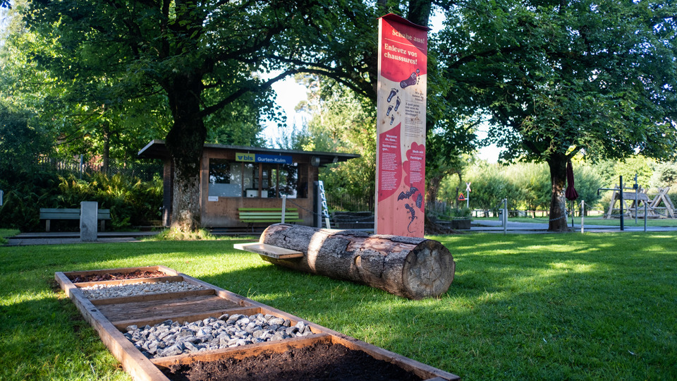 Un sentier pieds nus et une station du parcours découverte « Natur. Und du? » en arrière-plan.